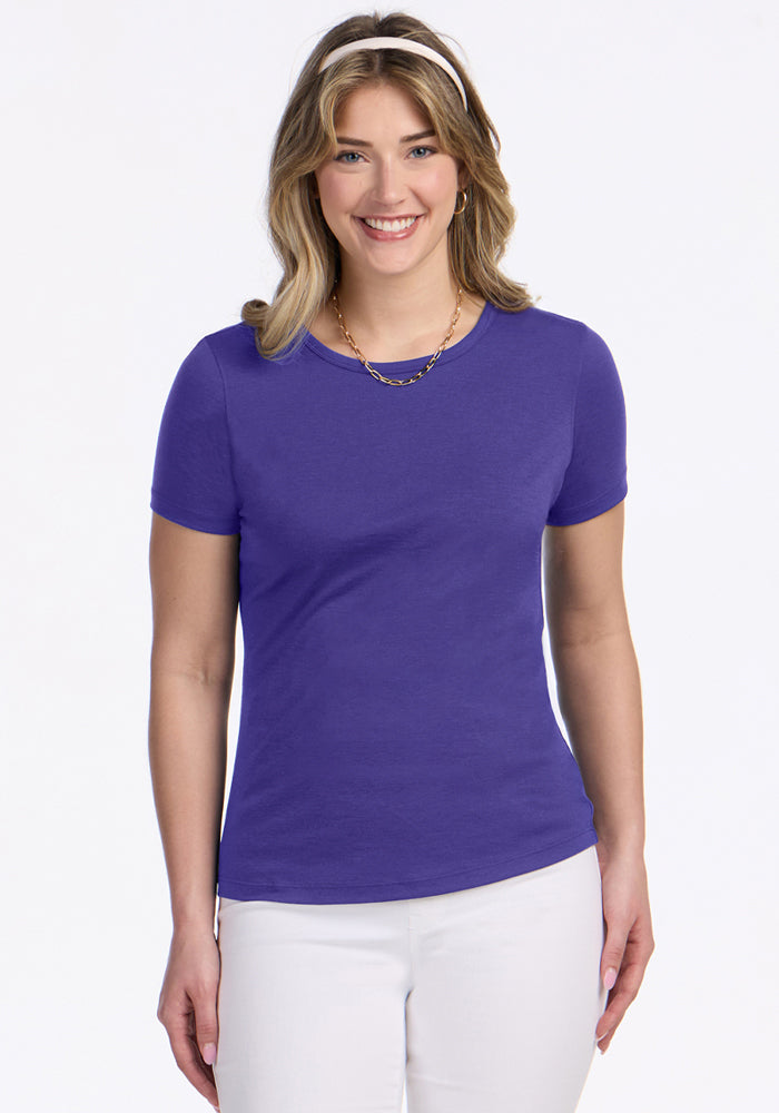 Woman smiling in a Woolx Liza Crew Neck Tee in Berry Indigo, white pants, and gold necklace against a white background. | Ariana is 5'11", wearing a size S