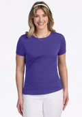 Woman smiling in a Woolx Liza Crew Neck Tee in Berry Indigo, white pants, and gold necklace against a white background. | Ariana is 5'11", wearing a size S
