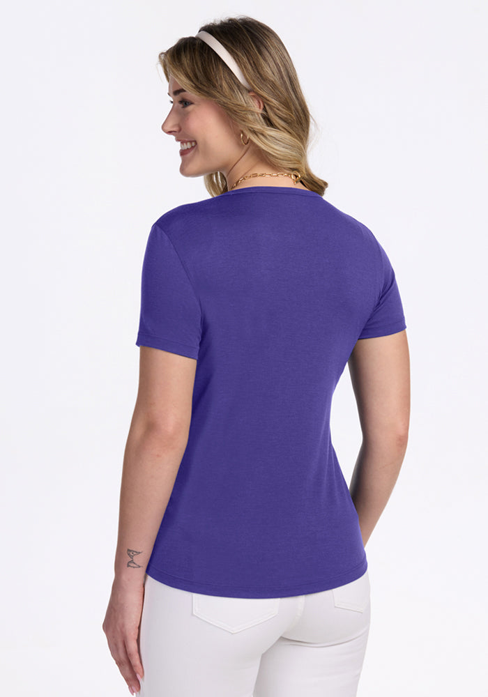 Woman facing away in Woolx Liza Crew Neck Tee - Berry Indigo, white pants, and a white headband on a light background.