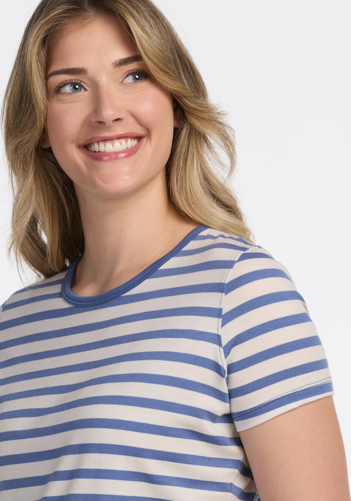 A blonde woman smiles while looking to the side, wearing the Woolx Liza Crew Neck Tee in Blue Sand Stripe against a plain white background.
