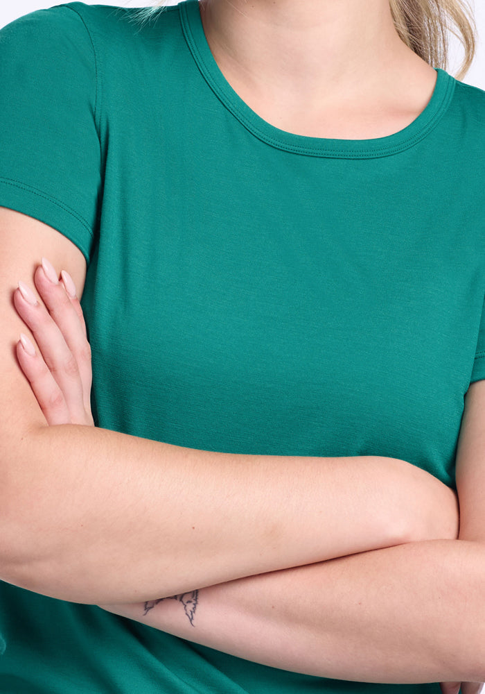 Wearing the Woolx Liza Crew Neck Tee in Cabana Crush, a person with crossed arms shows a small forearm tattoo.