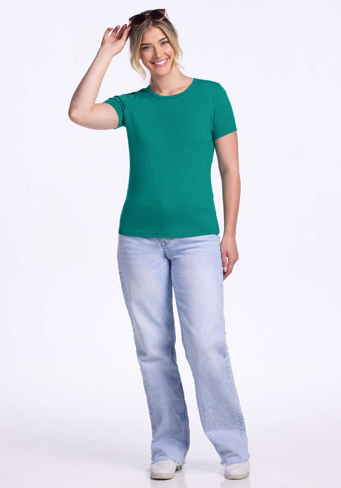 Smiling person in Woolx Liza Crew Neck Tee - Cabana Crush, light blue jeans, white shoes, sunglasses on head.