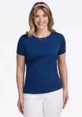 Woman smiling in a Woolx Liza Crew Neck Tee in Estate Blue, white pants, and gold necklace, on a white background.