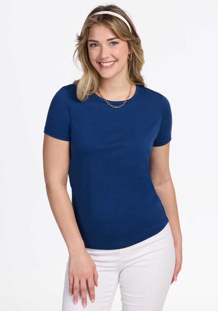 Smiling woman in Woolx Liza Crew Neck Tee • Final Sale - Estate Blue and white pants, standing against a white background.
