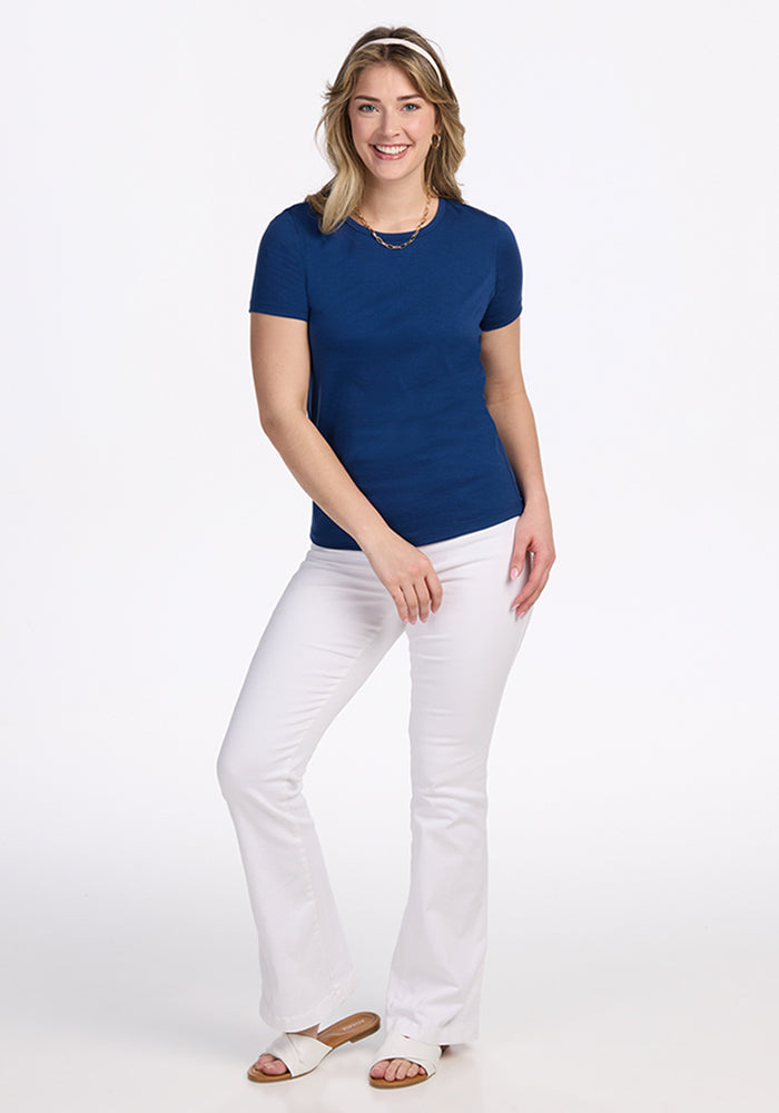 Woman smiling, wearing the Woolx Liza Crew Neck Tee in Estate Blue, with white pants and sandals against a white background.