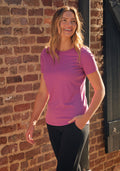 Woman smiling outdoors in a Woolx Liza Crew Neck Tee in Purple Wine and black pants, brick wall behind her.