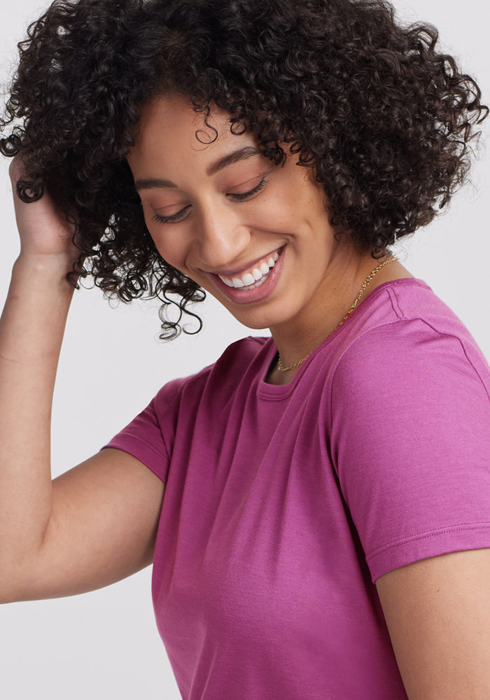 Smiling woman with curly hair, wearing Woolx Liza Crew Neck Tee in Purple Wine and a gold necklace. Final Sale.