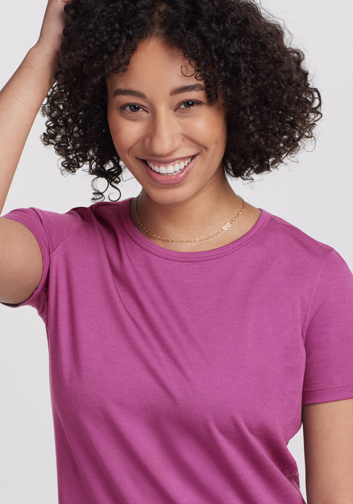 Smiling woman in the Woolx Liza Crew Neck Tee • Final Sale - Purple Wine, touching her head against a plain background.