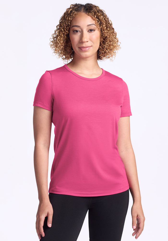 Woman with curly hair wears the Woolx Liza Crew Neck Tee in Raspberry Fizz and black pants against a white background.