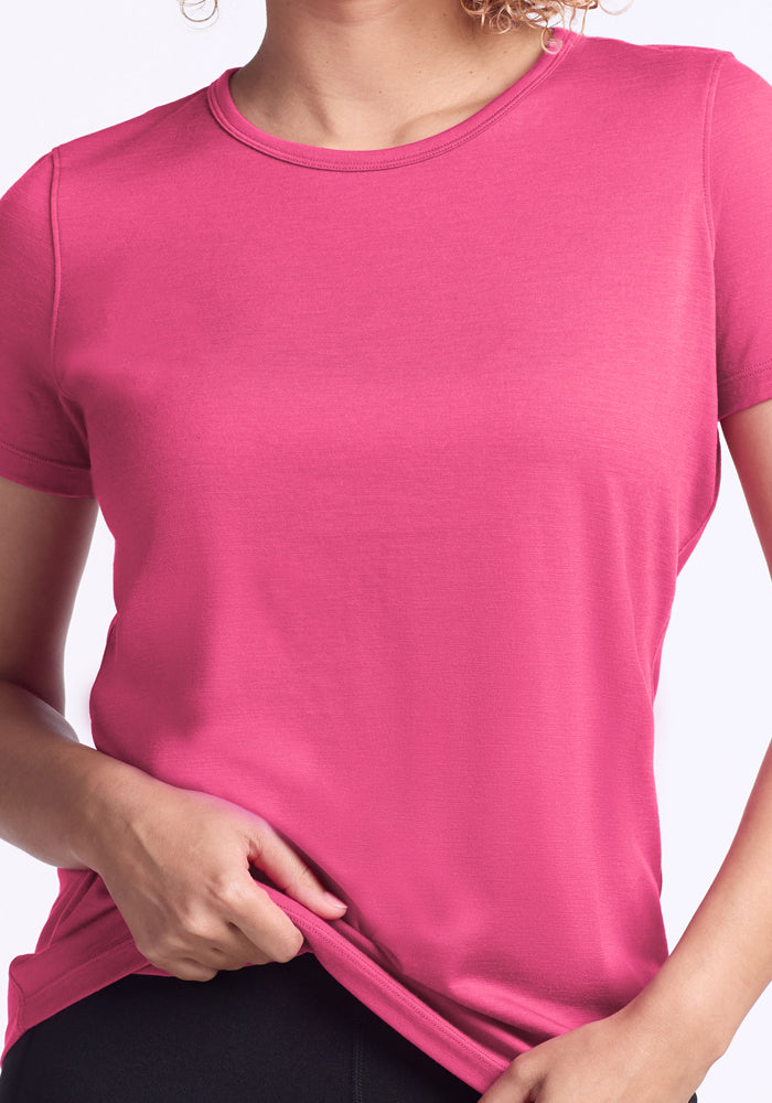 Woman in a Woolx Liza Crew Neck Tee in Raspberry Fizz holds the shirt hem with one hand.