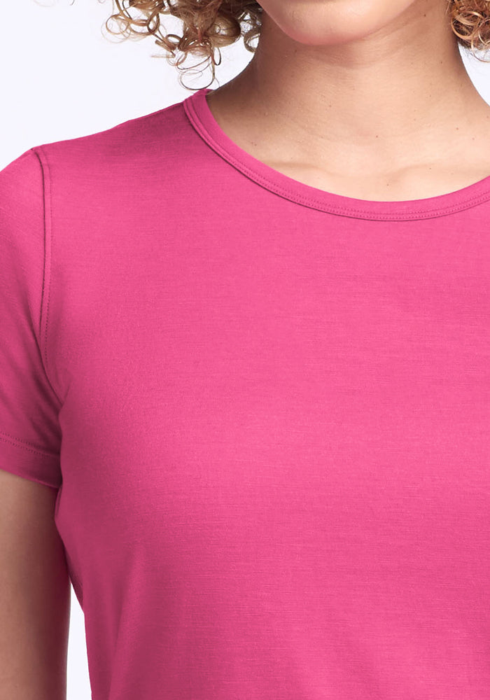Person wearing a Woolx Liza Crew Neck Tee in Raspberry Fizz, shown from shoulders to upper chest with partial curls visible.