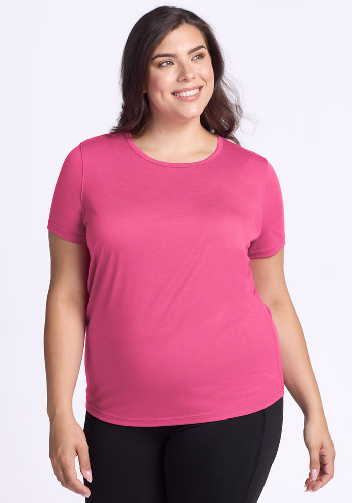 Woman with long brown hair smiles in the Woolx Liza Crew Neck Tee in Raspberry Fizz and black pants, white background.
