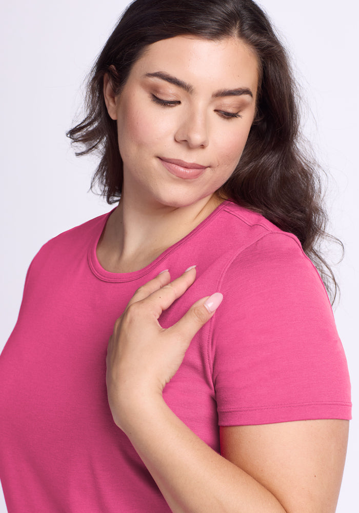 Woman with long brown hair in the Woolx Liza Crew Neck Tee in Raspberry Fizz, looking down and touching her shoulder.