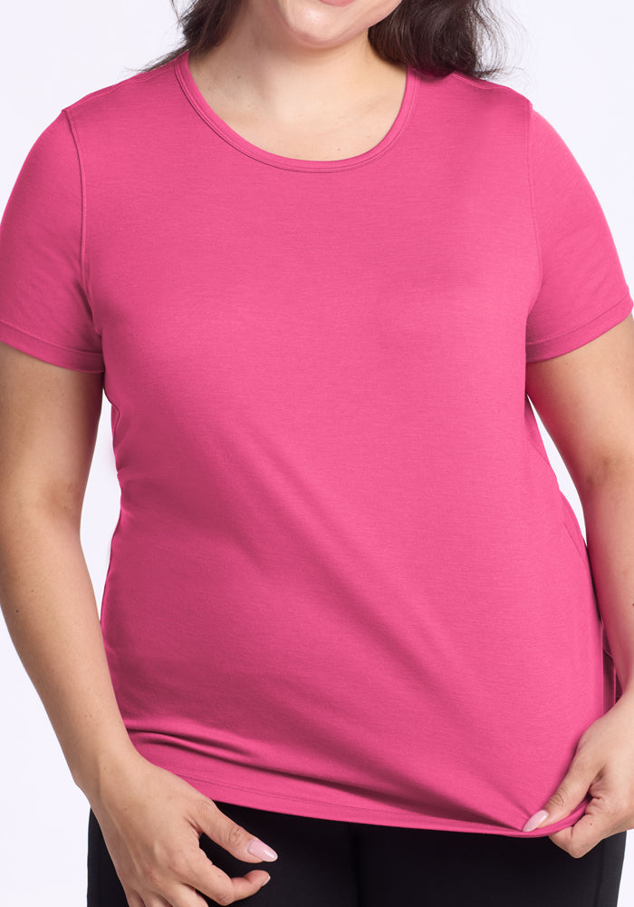 A woman in a Woolx Liza Crew Neck Tee in Raspberry Fizz and black pants holds the hem of her shirt.
