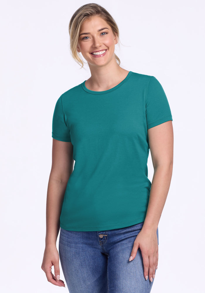 Smiling woman in Woolx Liza Crew Neck Tee in Surfside and jeans stands against a plain white background.