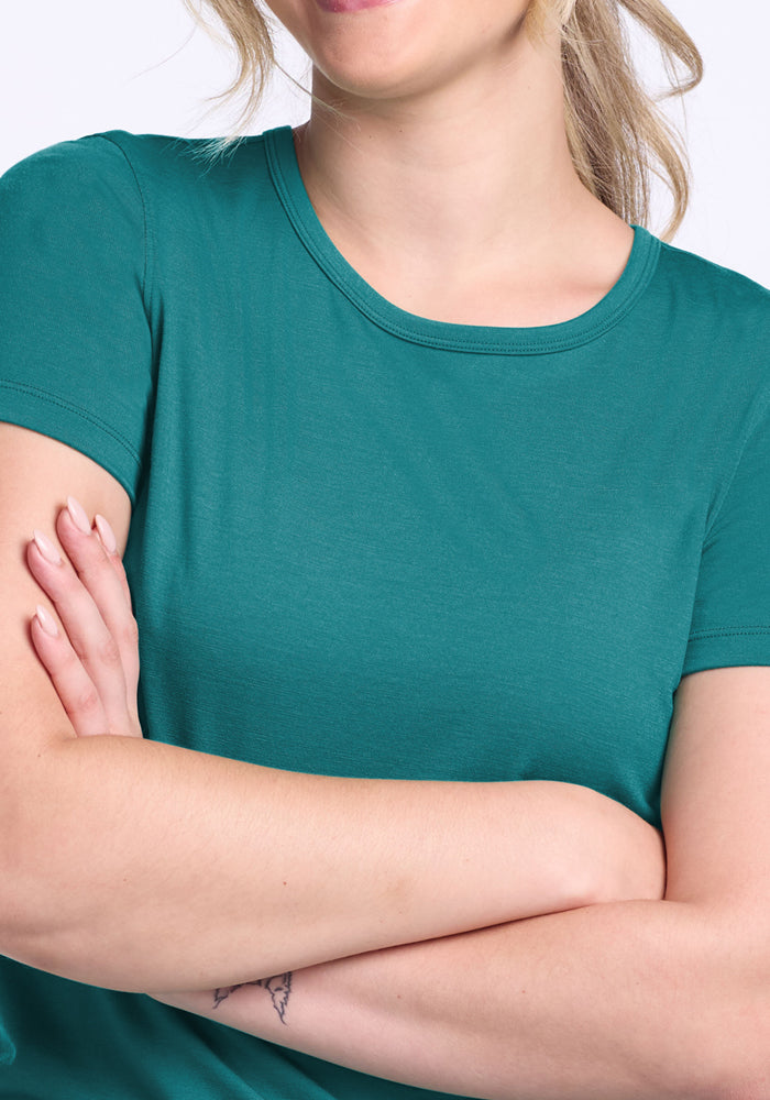 Woman in a Woolx Liza Crew Neck Tee in Surfside, arms crossed, small wrist tattoo, smiling against plain background.