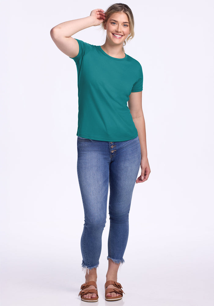 Smiling woman in the Woolx Liza Crew Neck Tee – Surfside, blue jeans, and sandals against a white background.