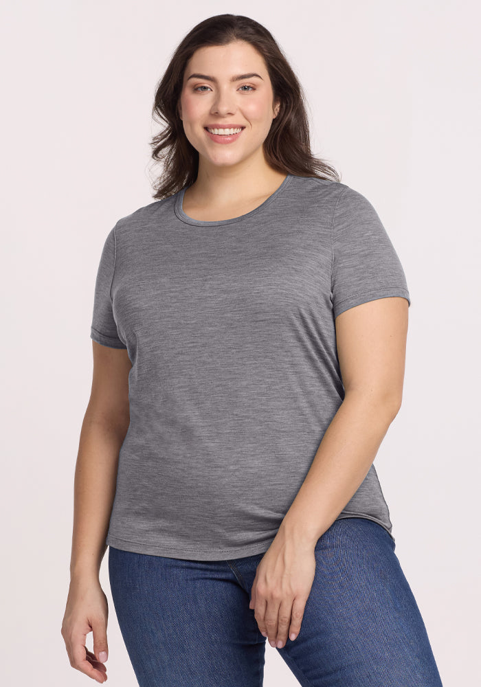A person wearing the Woolx Liza Crew Neck Tee in Graphite Heather and blue jeans smiles while standing against a plain background. | Juliana is 5'10", wearing a size XL