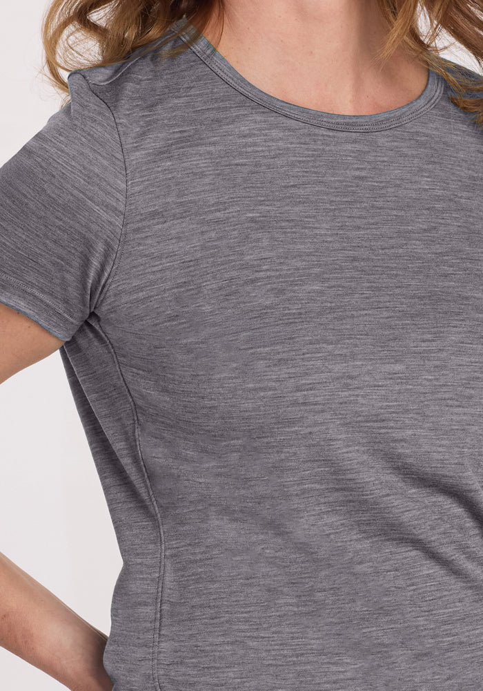 Wearing the Woolx Liza Crew Neck Tee in Graphite Heather, a person confidently stands with one hand on their hip. The lightweight Merino wool's performance benefits are clear in the sleek design, though their face is out of frame.