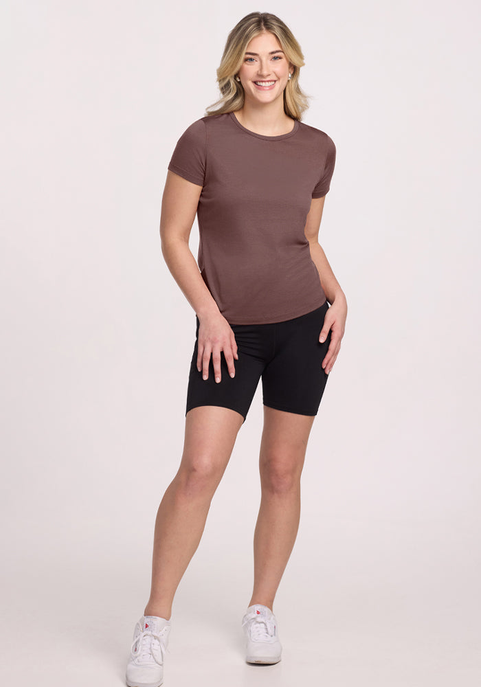 Smiling woman wears Woolx Liza Crew Neck Tee in Peppercorn and black shorts, posing with one hand on her hip.