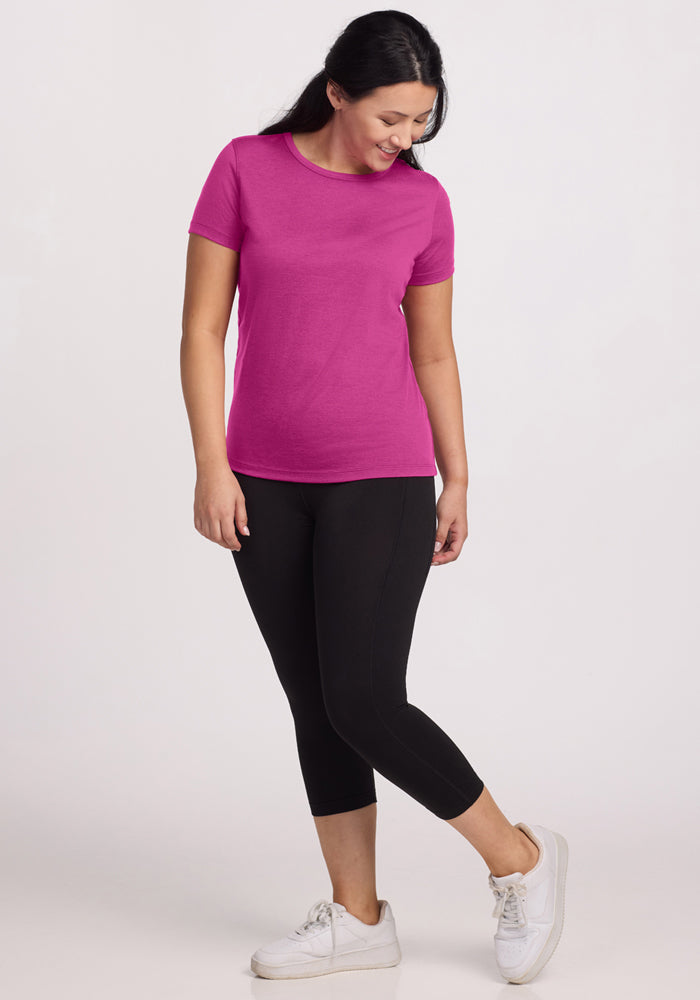 Woman smiling in a Woolx Liza Crew Neck Tee in Summer Sorbet, black leggings, and white sneakers on a light background.