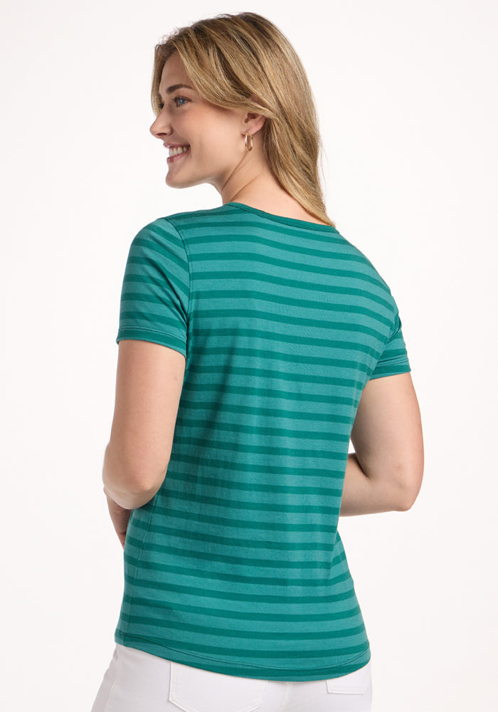 Smiling woman in a Woolx Liza Crew Neck Tee - Woodland Stripe and white pants, seen from the back against a plain background.