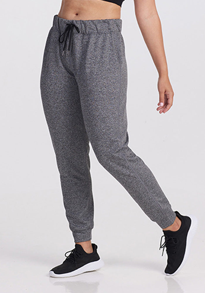 A person stands against a plain white background wearing Woolx Lola Jogger • Final Sale Deals! - Thunder Melange, featuring an elastic waistband with drawstring, paired with a black crop top and black athletic shoes.