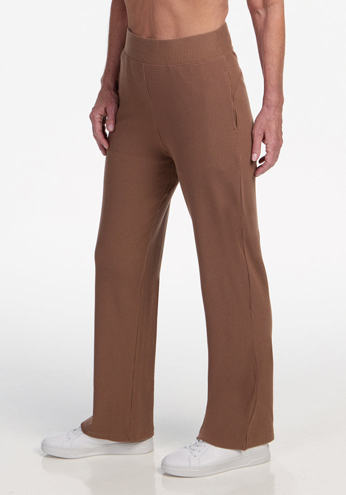 A person wearing Woolx Luca Ribbed Pants in Sienna Kiss with white sneakers stands against a plain white background. The image is cropped from the mid-torso down. | Tam is 5’8.5”, wearing a size S