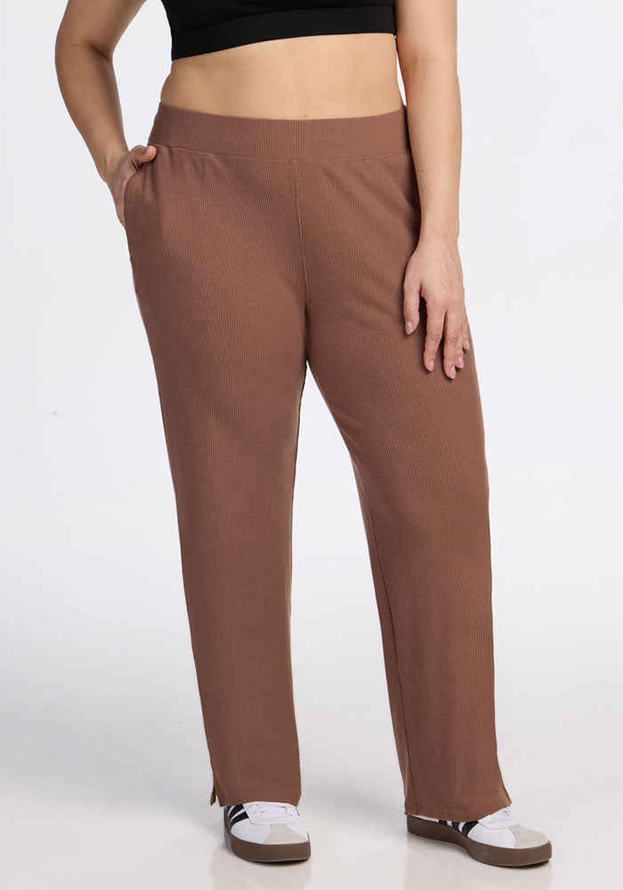 A person wearing a black crop top, Woolx Luca Ribbed Pants in Sienna Kiss with hands in pockets, and white sneakers stands against a plain white background. | Juliana is 5'10", wearing a size XL