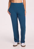 A person is wearing Woolx Luca Ribbed Pants in Moroccan Blue with white sneakers featuring brown soles. Their hands are in their pockets, shown waist down against a plain light background. | Ariana is 5'11", wearing a size S