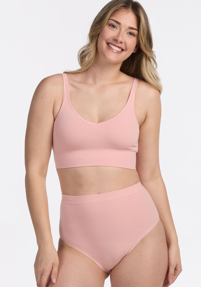 A smiling woman with long, wavy blonde hair models the Woolx Mabel Full Coverage Underwear in Rosewater, paired with a matching bralette, posing against a plain white background.