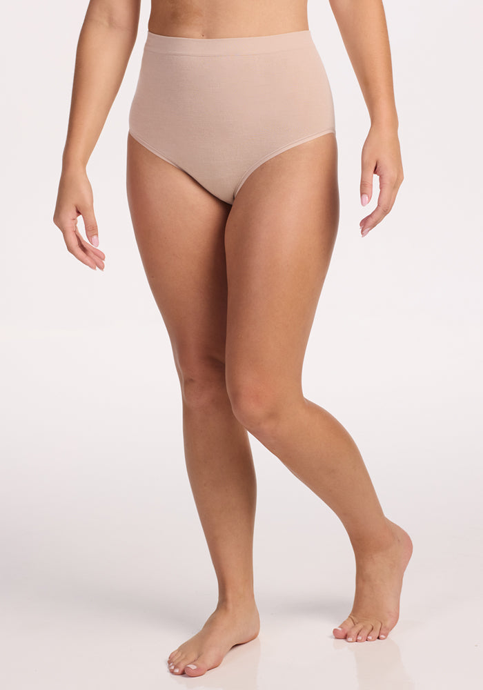 A person wearing Woolx Mabel Full Coverage Underwear in Sand stands barefoot against a plain white background, highlighting the seamless comfort. The image showcases the body from shoulders to feet.