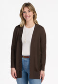 A blonde woman wearing the Woolx Macie Sweater - Bracken over a white shirt and blue jeans, smiling while standing against a plain white background. | Ariana is 5'11", wearing a size S