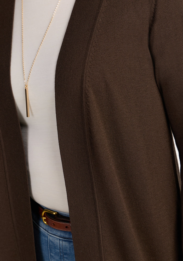 Close-up of a person wearing the Woolx Macie Sweater in Bracken over a white top, paired with blue jeans, a brown belt, and a rectangular gold pendant necklace.