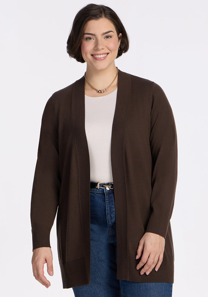 A woman with short dark hair smiles against a white background, wearing the Woolx Macie Sweater in Bracken over a white top and blue jeans, accessorized with a gold necklace. | Juliana is 5'10", wearing a size XL