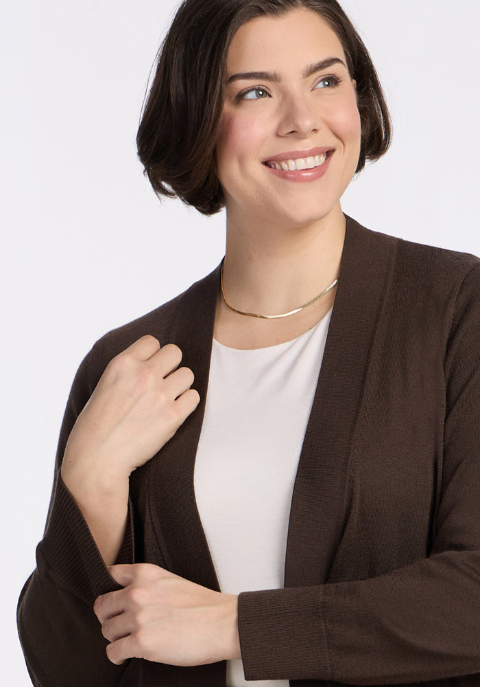 A woman with short brown hair wears a white top and the Woolx Macie Sweater in Bracken over a simple gold necklace, smiling and looking to the side against a plain light background.