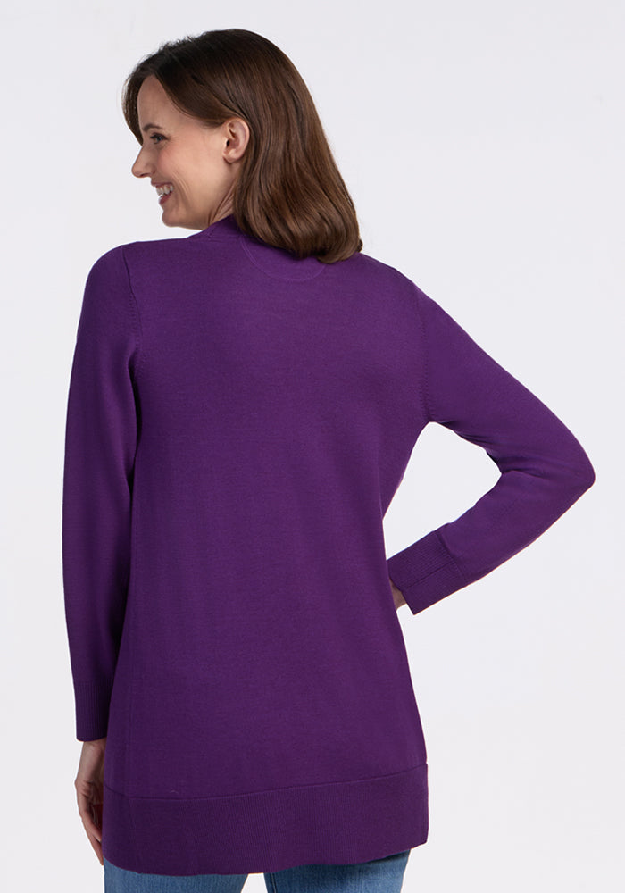 A woman with brown hair smiles with her back to the camera, wearing the Woolx Macie Sweater in Plum Crush and blue jeans against a plain white background.