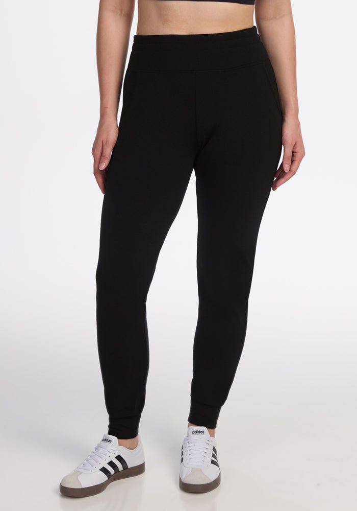 Someone wearing Madden Petite Joggers in black by Woolx and white Adidas sneakers with black stripes, standing against a plain white background. The image is cropped at the waist and ankles.