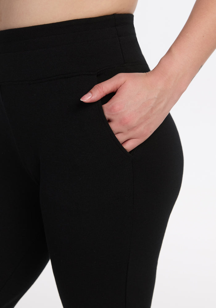 A person models Woolx Madden Petite Joggers in black, with their right hand in the pocket. The close-up image, cropped from waist to mid-thigh, highlights the joggers’ fit and waistband details.