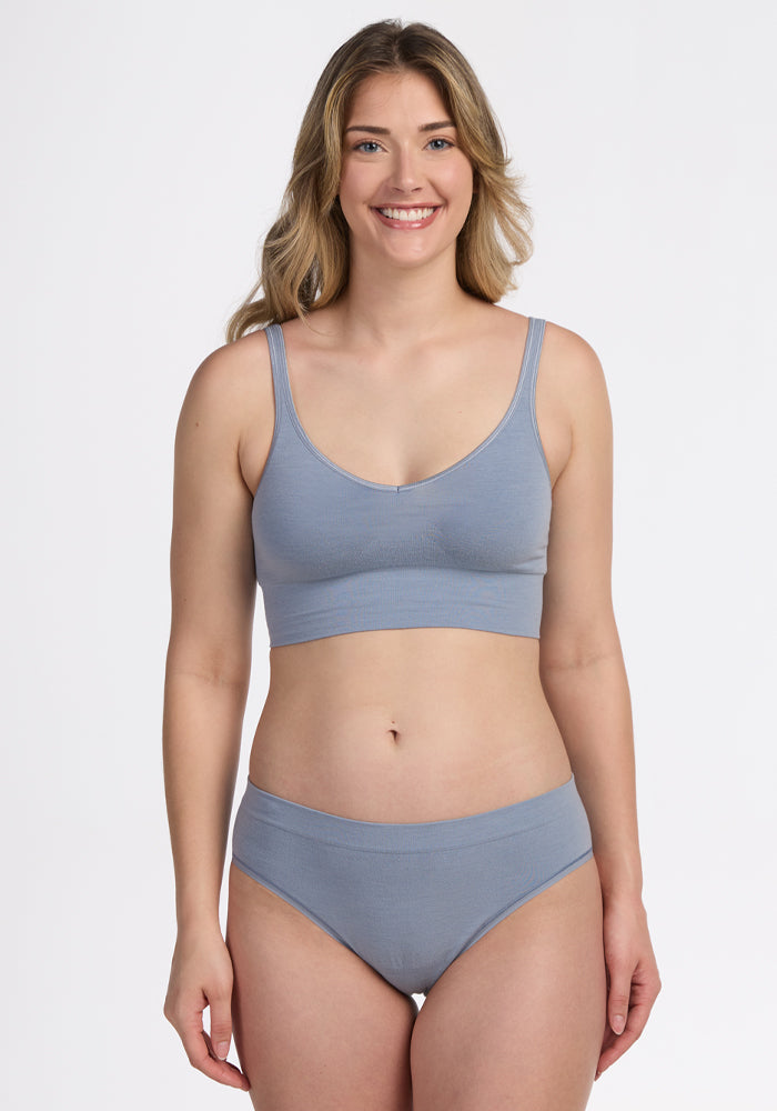 A woman with long, wavy blonde hair is smiling against a plain white background, wearing the Woolx Maeve Bikini in Bluebell.