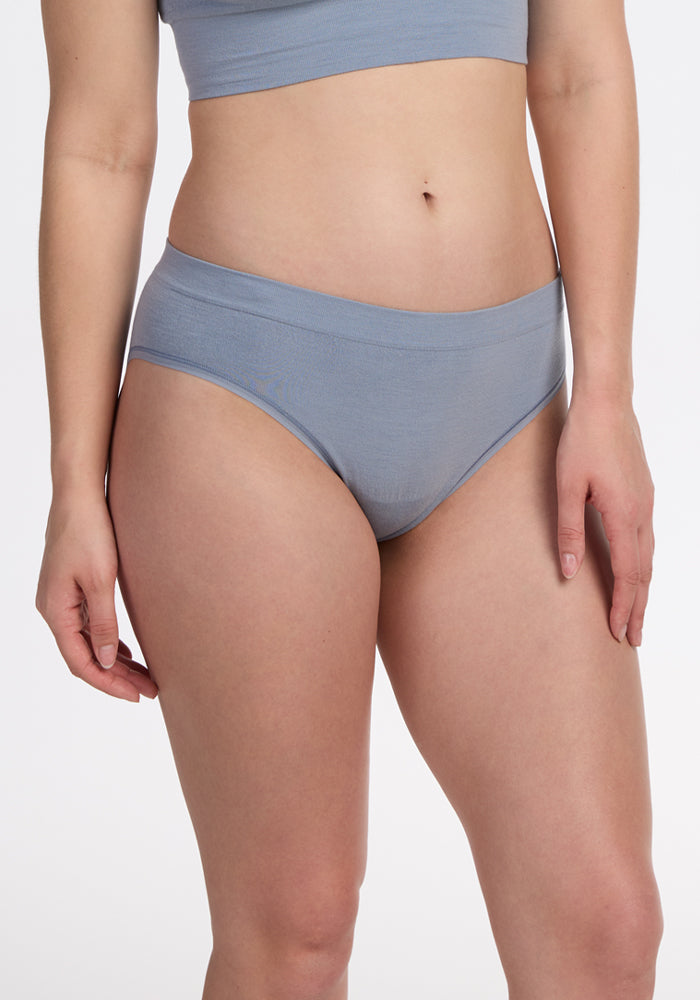 A woman models the Woolx Maeve Bikini in Bluebell, standing against a plain white background. The image highlights her torso and hips, with arms relaxed at her sides.