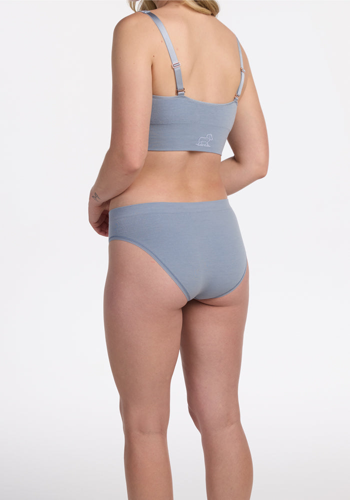 A woman faces away wearing the Woolx Maeve Bikini in Bluebell. Set against a plain white background, her back, arms, legs, and neck are shown, highlighting the bikini’s comfortable, moisture-wicking design.