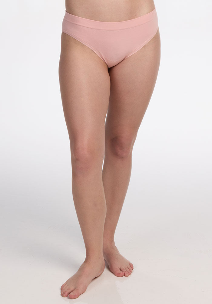 A person stands barefoot on a white background, wearing the Woolx Maeve Bikini in Rosewater. The image captures the body from mid-torso to feet, with arms not visible.