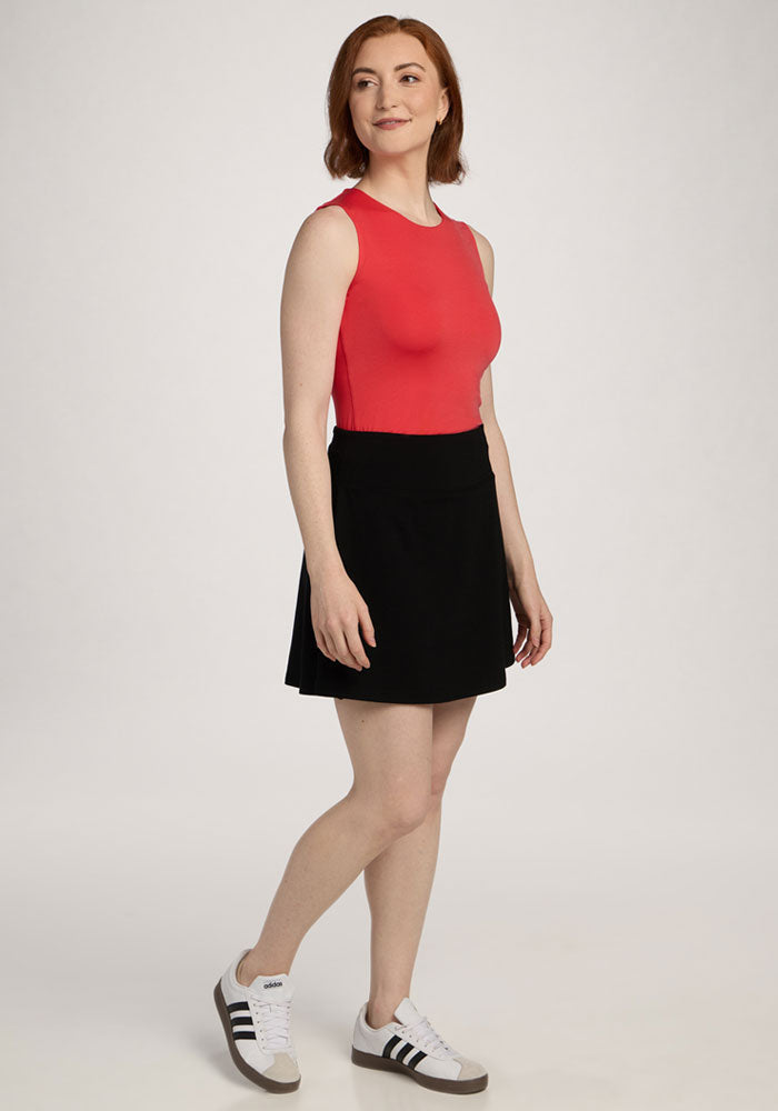 Person with short red hair wearing the Woolx Maggie Bodysuit in Hibiscus, black skirt, and white sneakers, smiling.