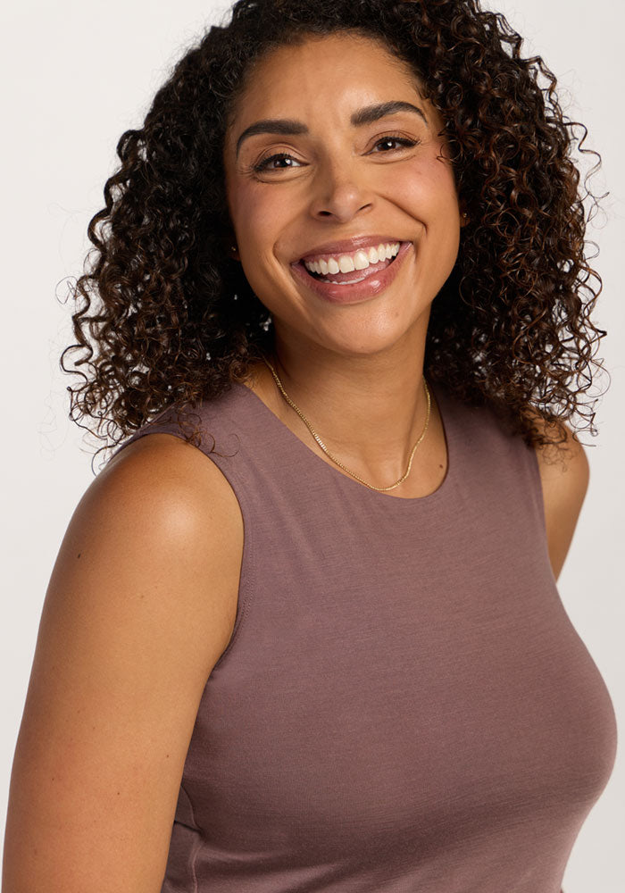 Smiling woman in the Woolx Maggie Bodysuit - Peppercorn, facing the camera, wearing a gold necklace.