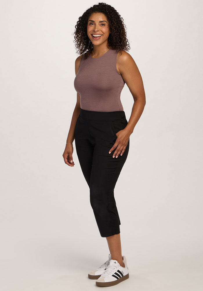 Smiling woman wears the Maggie Bodysuit in Peppercorn by Woolx with black cropped pants and sneakers.