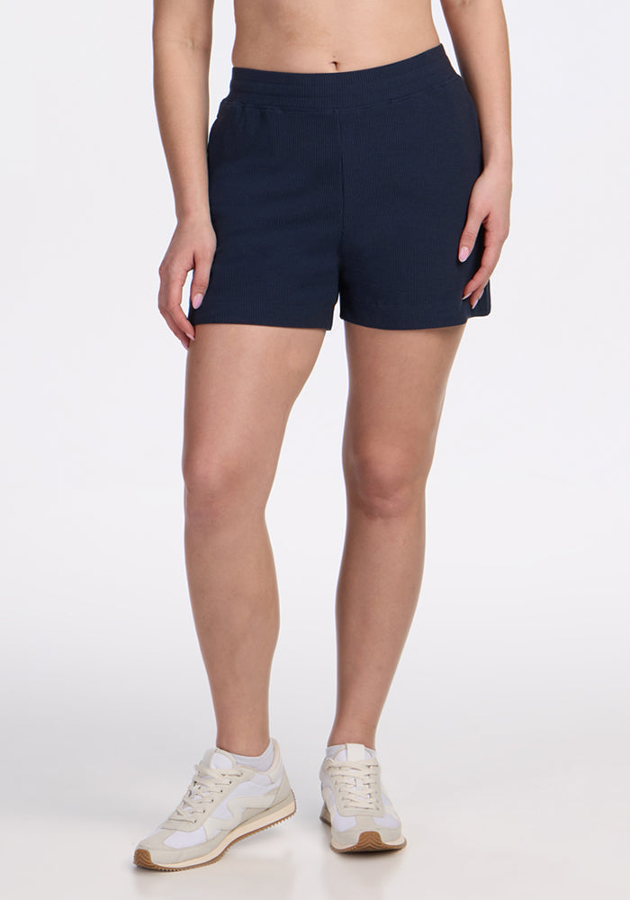Person wearing Woolx Maisey Ribbed Shorts in Deep Navy and white sneakers, standing against a white background.