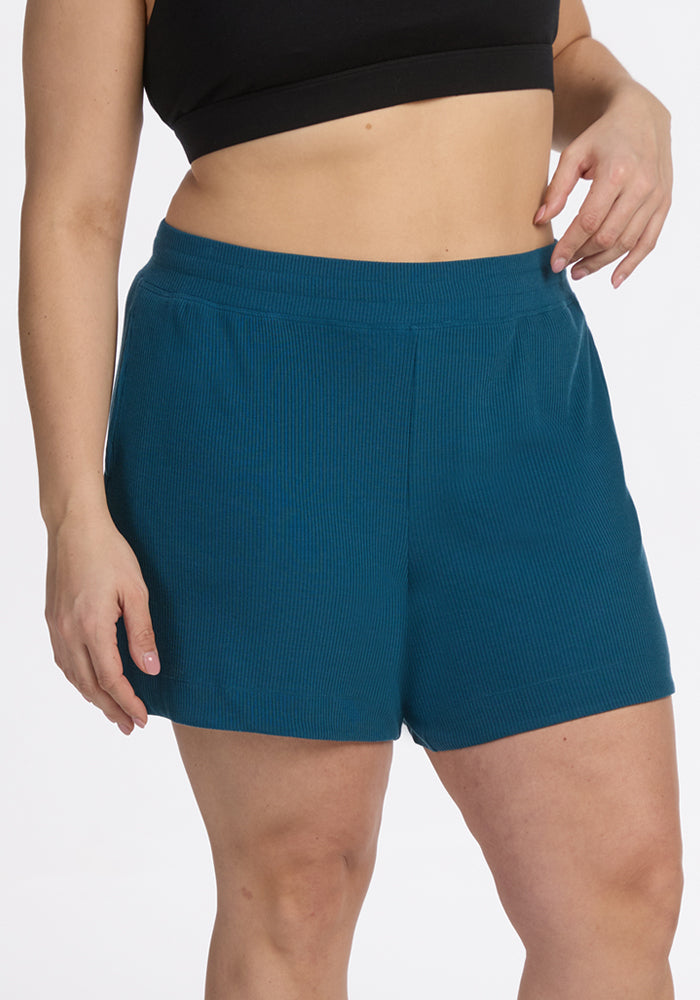 Model in Moroccan Blue Maisey Ribbed Shorts by Woolx, posing with hand on hip against a plain background.