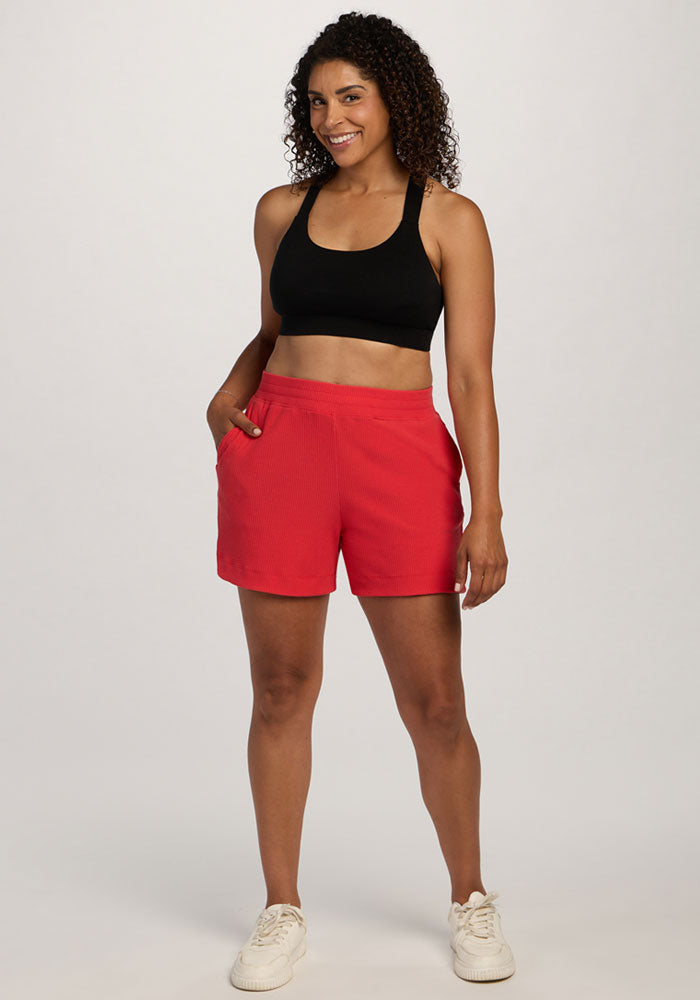 Woman in a black sports bra and Woolx Maisey Ribbed Shorts - Hibiscus, smiling against a plain background. | Kisha is 5'8", wearing a size M