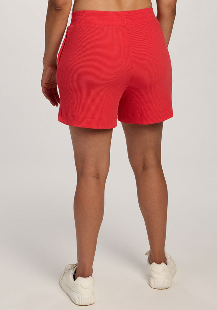 Person facing away, wearing Woolx Maisey Ribbed Shorts in Hibiscus and white sneakers on a plain, light background.